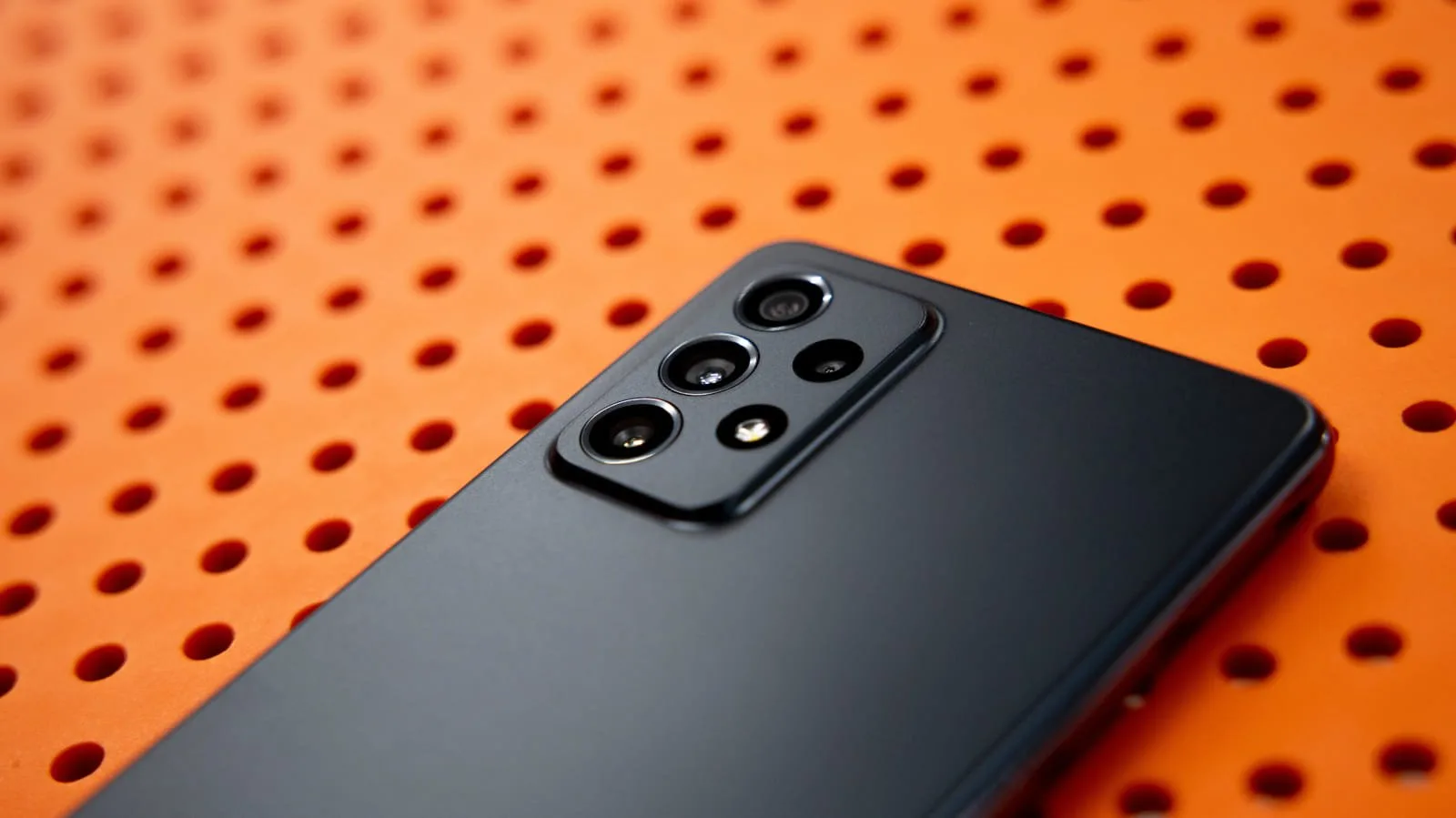 بخش پشتی یک تلفن همراه سیاه‌رنگ با چند دوربین دیده می‌شود. زمینه‌ی عکس نارنجی و دارای سوراخ‌های منظم است که ظاهر مدرن و چشم‌گیری به تصویر داده است.