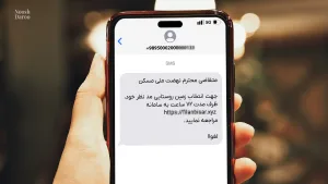 ، یک دست گوشی موبایلی را نگه داشته که یک پیامک با مضمون مرتبط با “نهضت ملی مسکن” بر روی صفحه آن نمایش داده شده است. متن پیامک شامل اطلاعاتی درباره انتخاب زمین روستایی در مدت زمان ۷۲ ساعت و لینکی برای مراجعه به سامانه است.