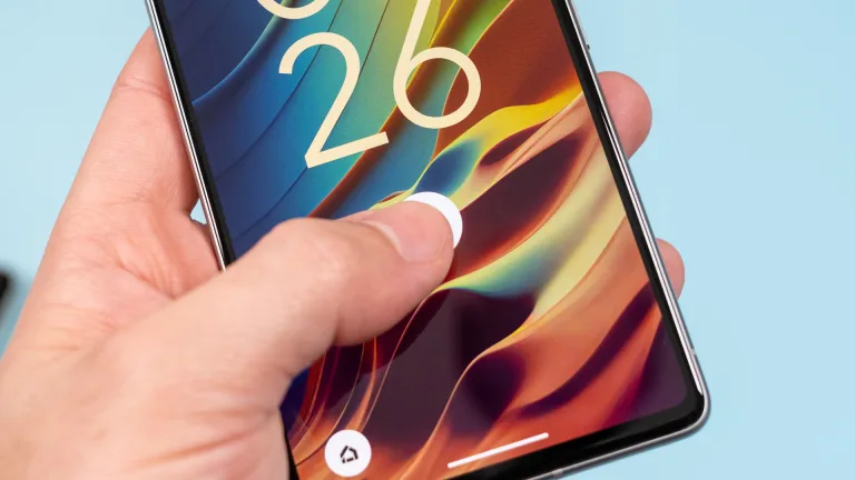 تصویری از یک موبایل در دست فردی که انگشت شست خود را روی حسگر اثر انگشت در میانه‌ی نمایشگر گذاشته است.