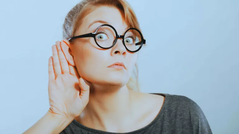 زن با عینک دایره‌ای و دست کنار گوش، نماد استراق سمع.
