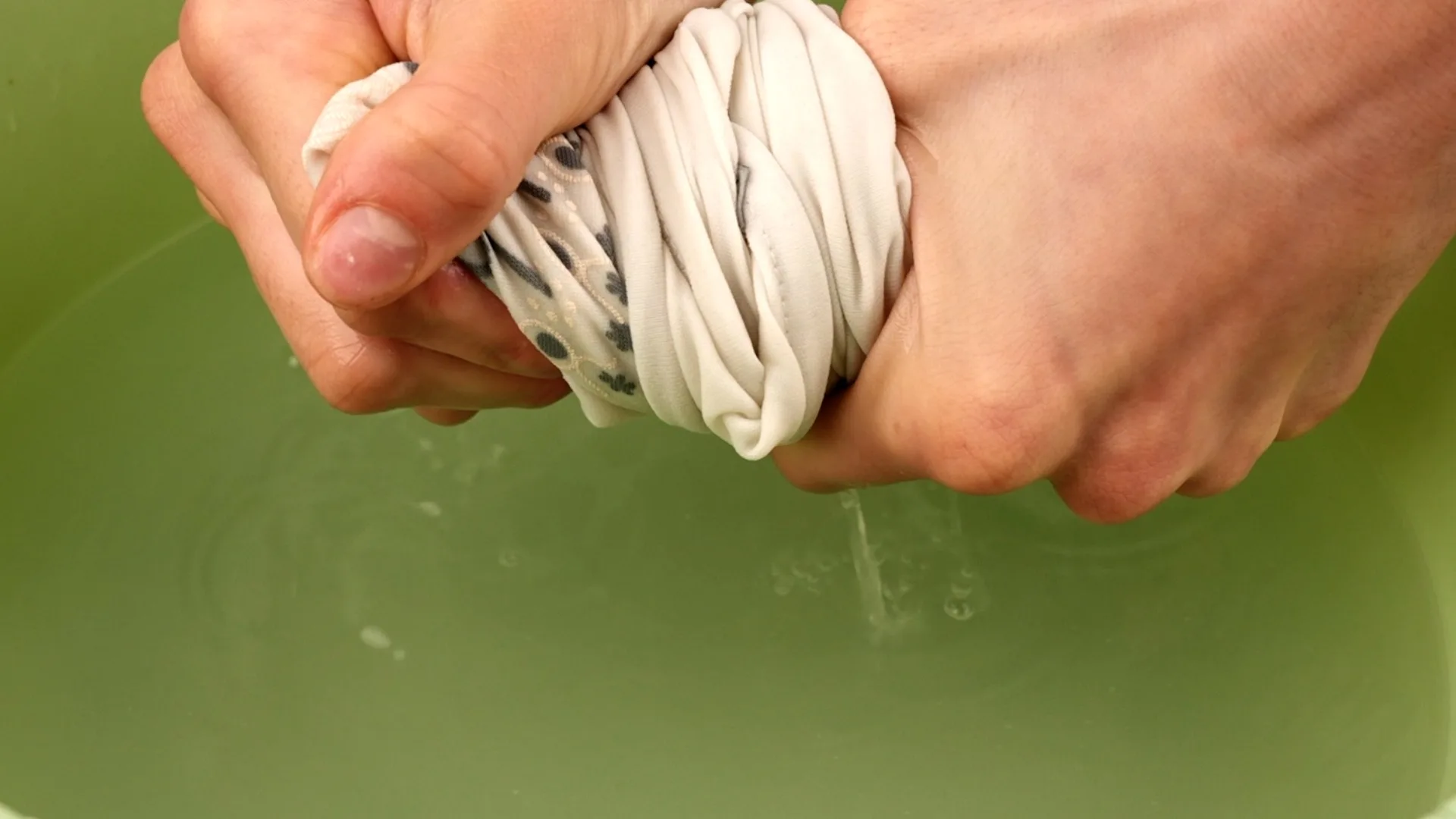 دستها پارچهای روشن را بالای لگن آب میفشارند و میچلانند.