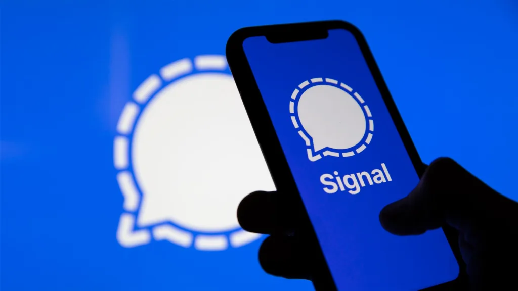 سایه دستی که یک گوشی هوشمند با لوگوی پیام‌رسان سیگنال را در برابر پس‌زمینه‌ای آبی نگه داشته است