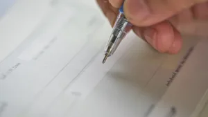 نمای نزدیک از دست فردی که آماده نوشتن روی یک چک بانکی است.