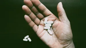 چند قرص سفید در کف دست یک فرد روی پس‌زمینه تاریک.