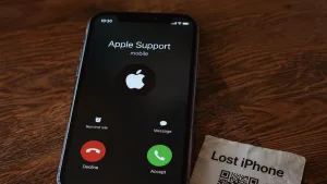 آیفونی روی میز چوبی که تماس ورودی با نام Apple Support را نشان می‌دهد و کنارش کاغذی با نوشته Lost iPhone و یک کد QR قرار دارد؛ نمادی از تماس جعلی پشتیبانی اپل پس از سرقت گوشی